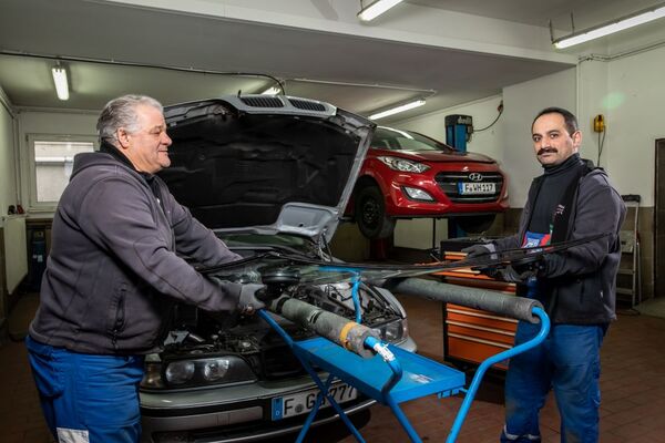 Zwei Kfz-Mechaniker wechseln in einer Autowerkstatt gemeinsam eine Windschutzscheibe.