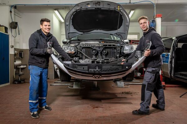 Zwei Kfz-Mechaniker reparieren gemeinsam die Stoßstange eines Volkswagen in der Werkstatt.