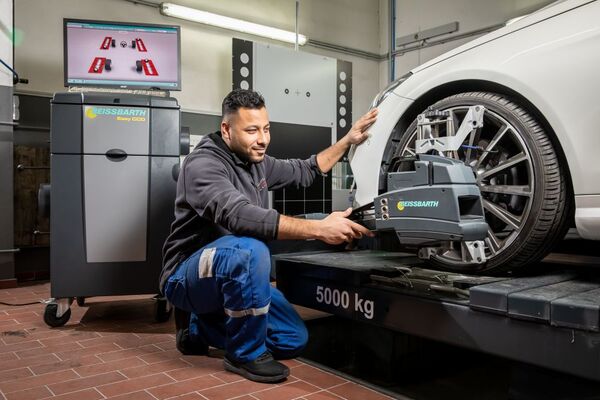 Mechaniker prüft mit Achsvermessungsgerät die Spur eines Autos in moderner Werkstatt.