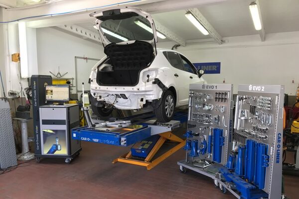 Ein weißes Auto steht in einer Werkstatt auf einer Hebebühne zur Karosseriereparatur.