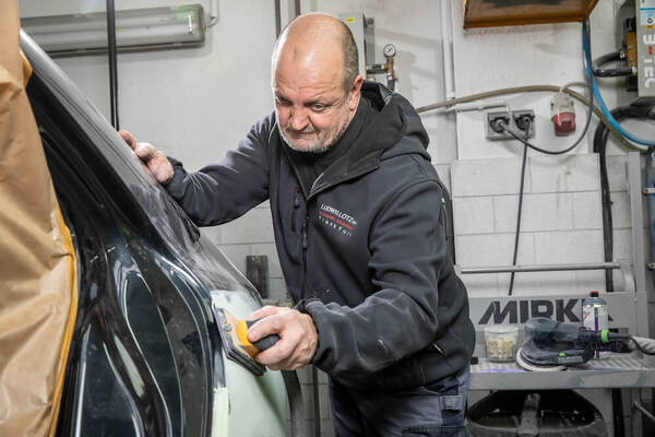 Ein Automechaniker schleift in einer Werkstatt die Karosserie eines Fahrzeugs ab.